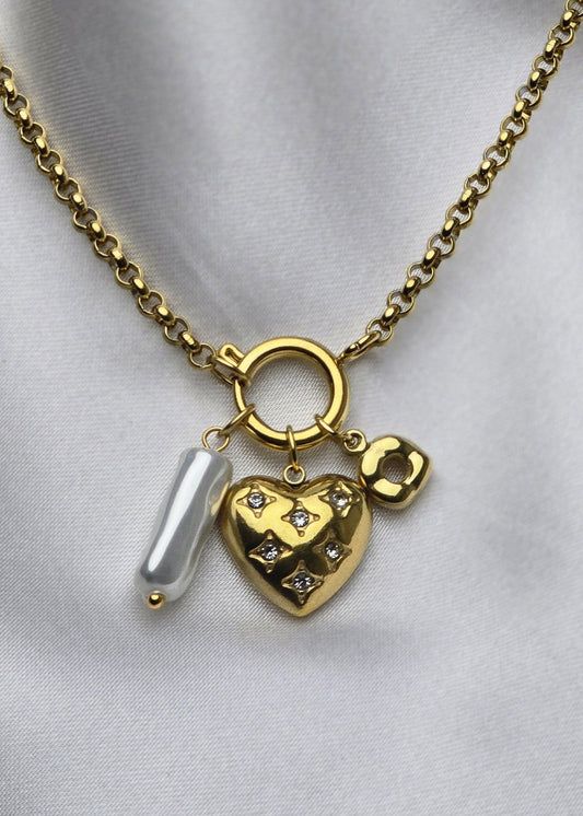 Gold necklace with a heart-shaped pendant on a light gray fabric background